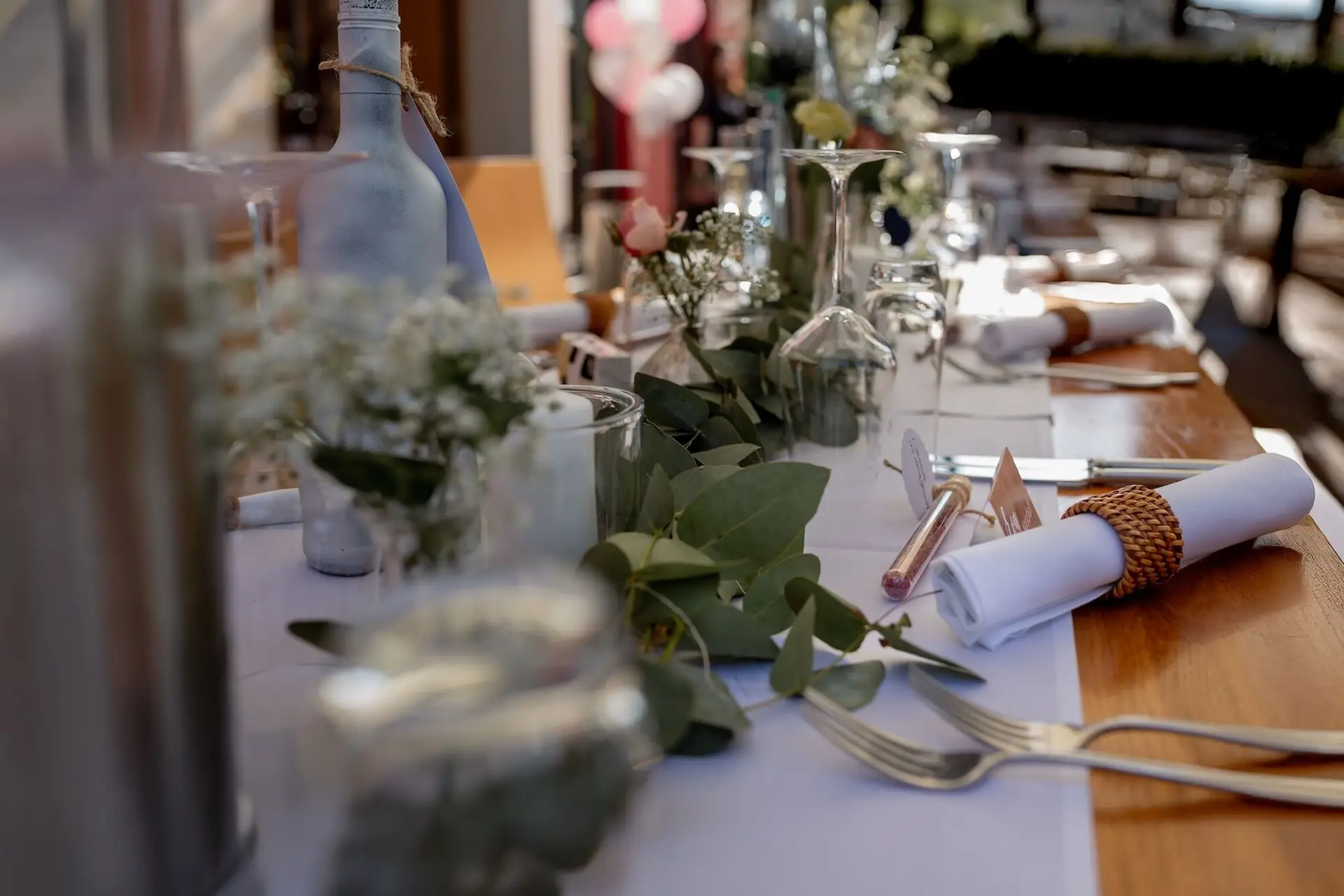 Festlich gedeckter Tisch mit Blumen und Gläsern, Gäste und pinke Luftballons im Hintergrund