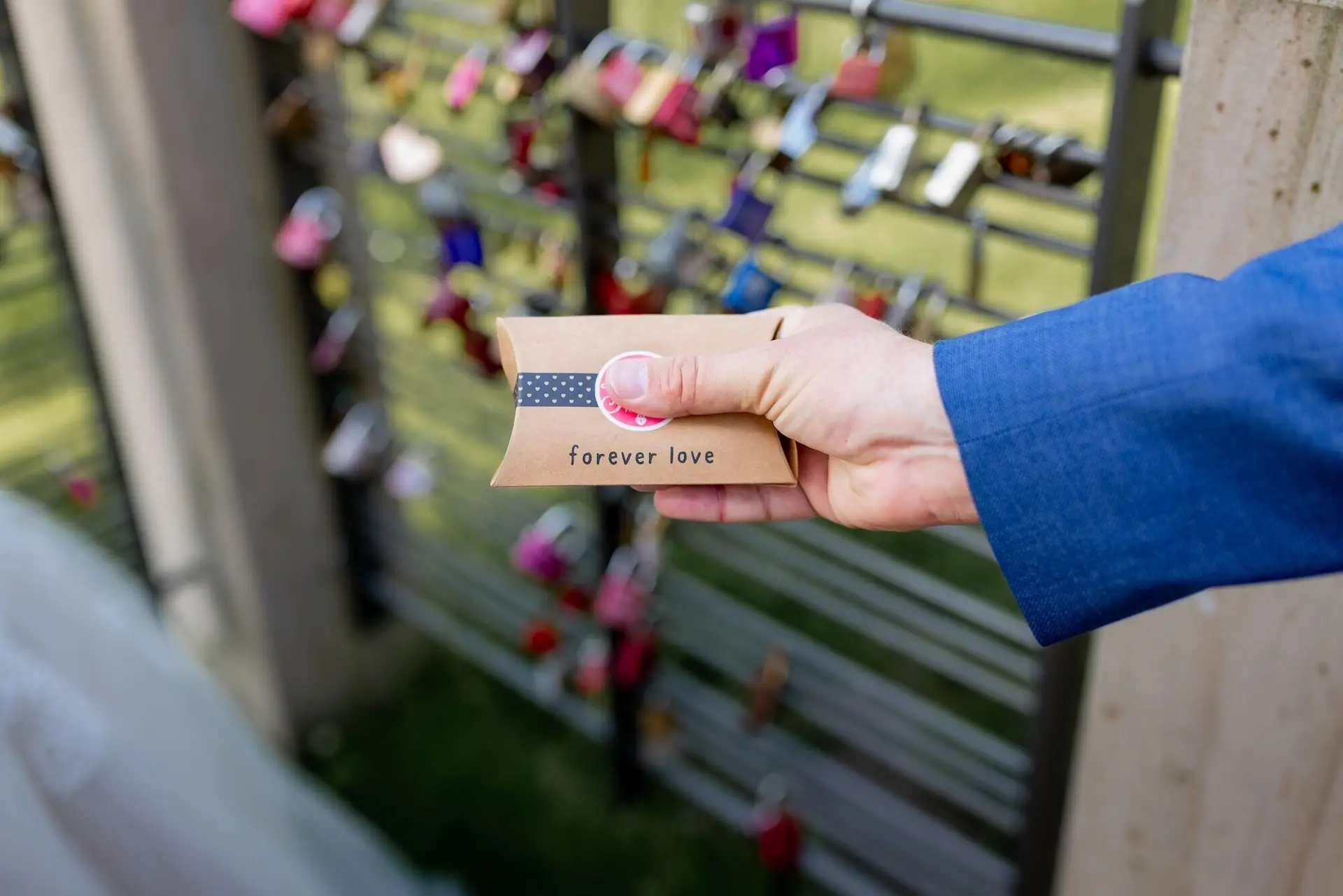 Hand hält kleine 'forever love'-Karte vor dem Liebesschloss-Geländer im Kurpark Bad Dürkheim