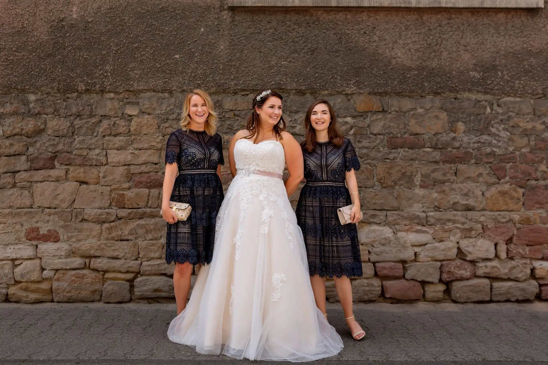 Braut mit zwei Brautjungfern lächelt vor historischem Steingebäude im Ortskern Mutterstadt