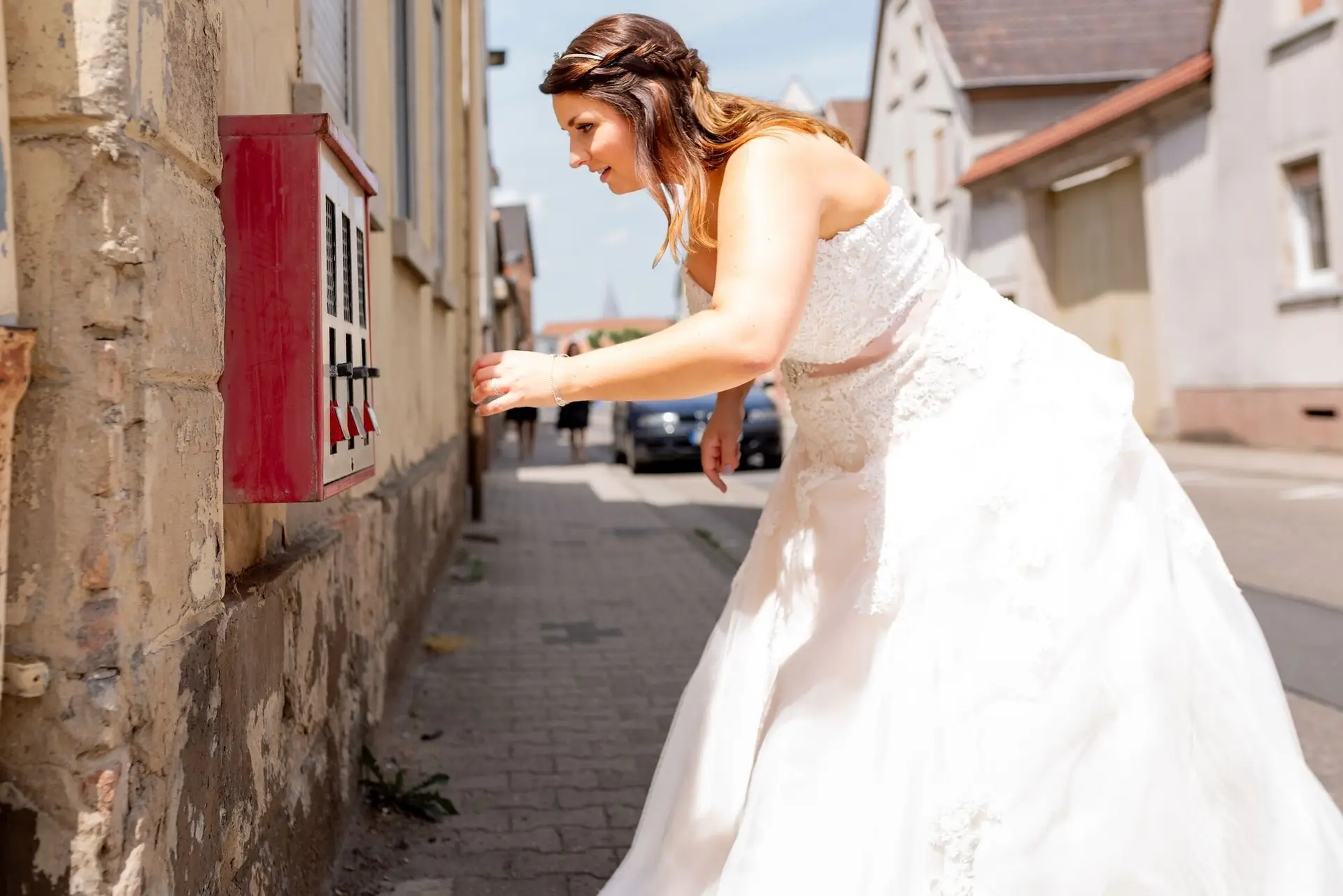 Braut im weißen Kleid spielt mit einem roten Kaugummiautomaten in der Gasse von Mutterstadt