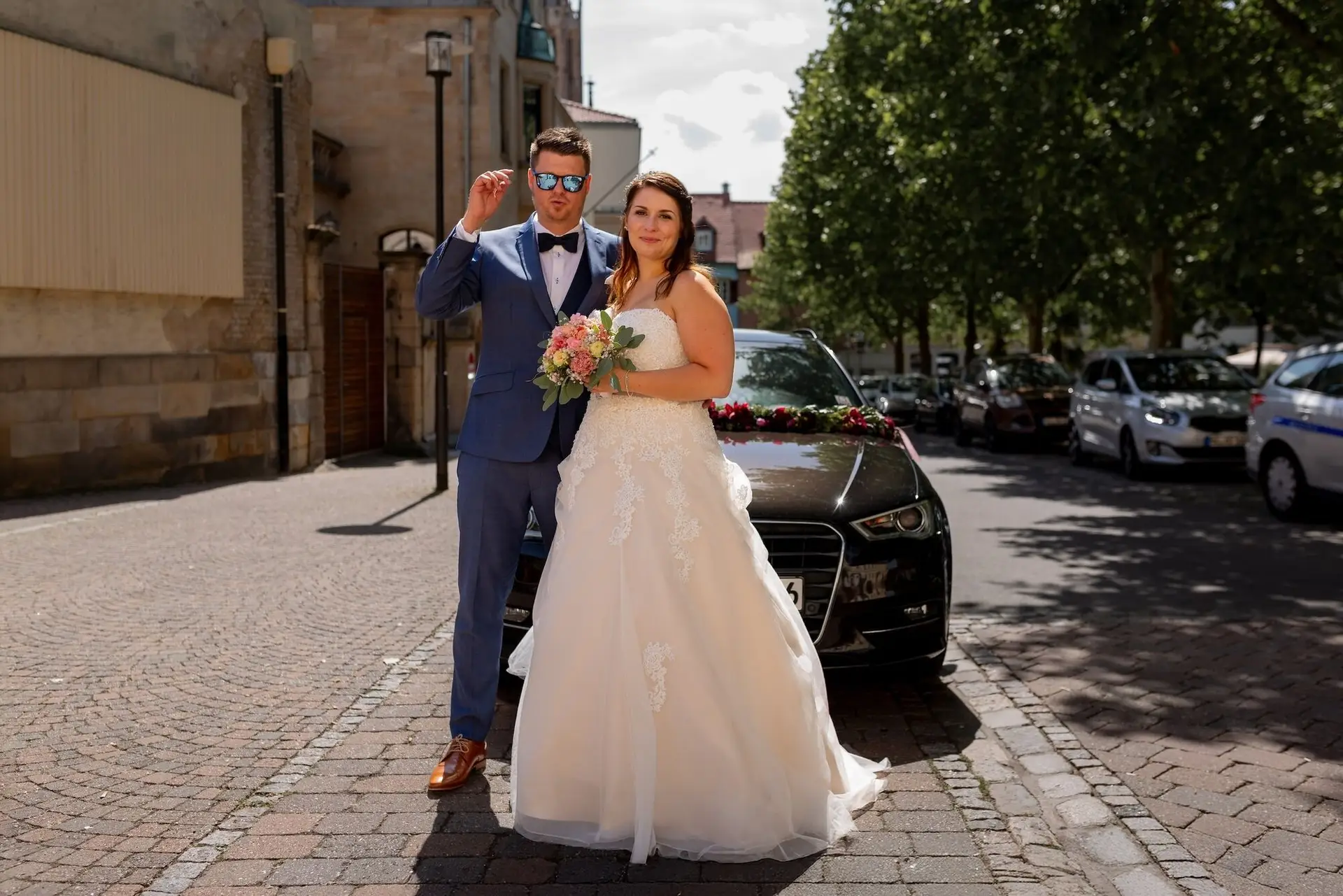 Brautpaar vor schwarzem Hochzeitsauto auf gepflasterter Straße nach der Trauung in Mutterstadt