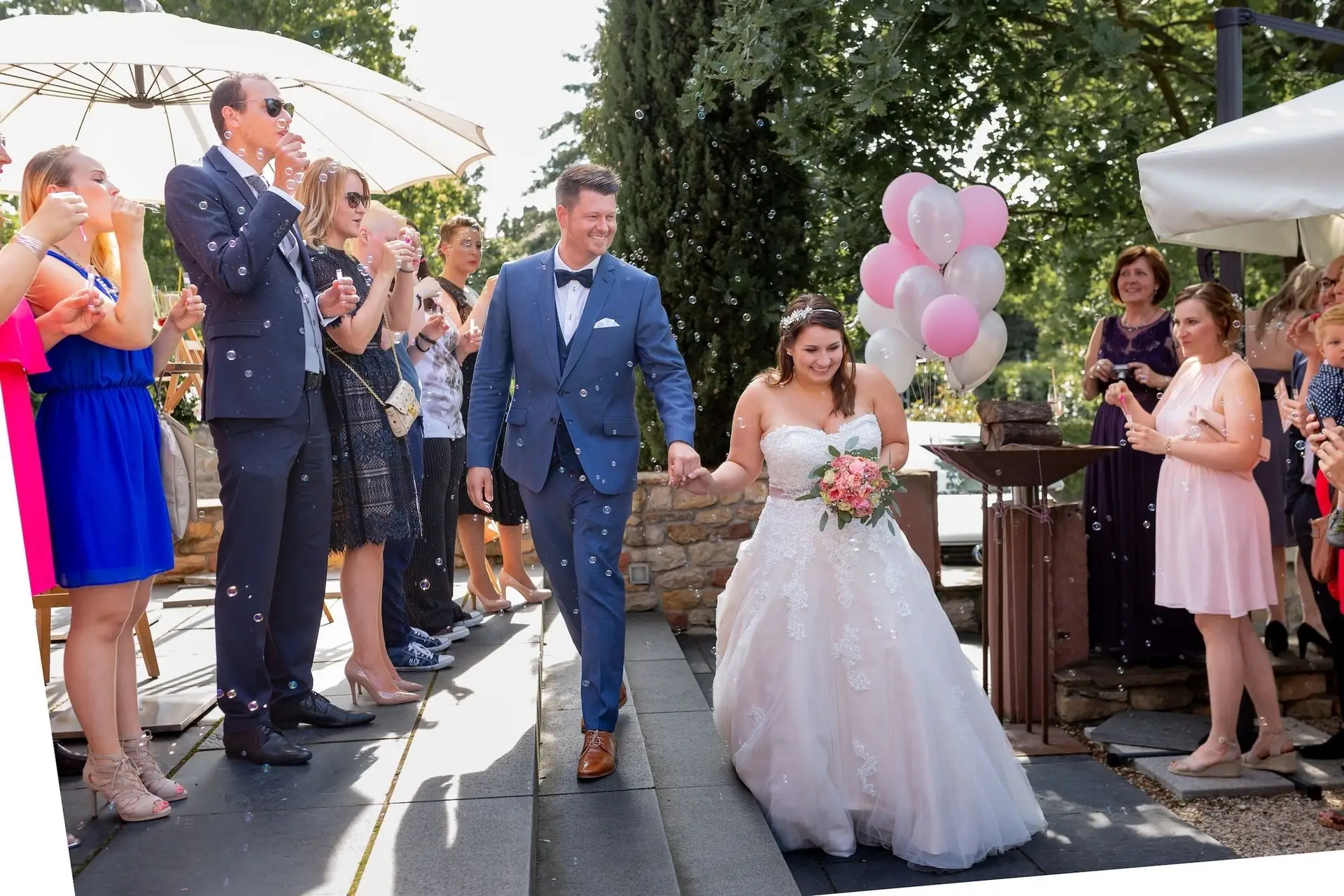 Brautpaar schreitet durch Seifenblasen auf der Straße, Gäste applaudieren beim Auszug nach der Trauung