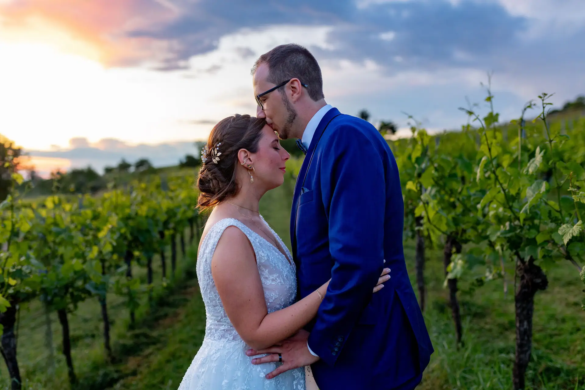 Bräutigam küsst seine Braut sanft auf die Stirn im Weinberg bei Abenddämmerung