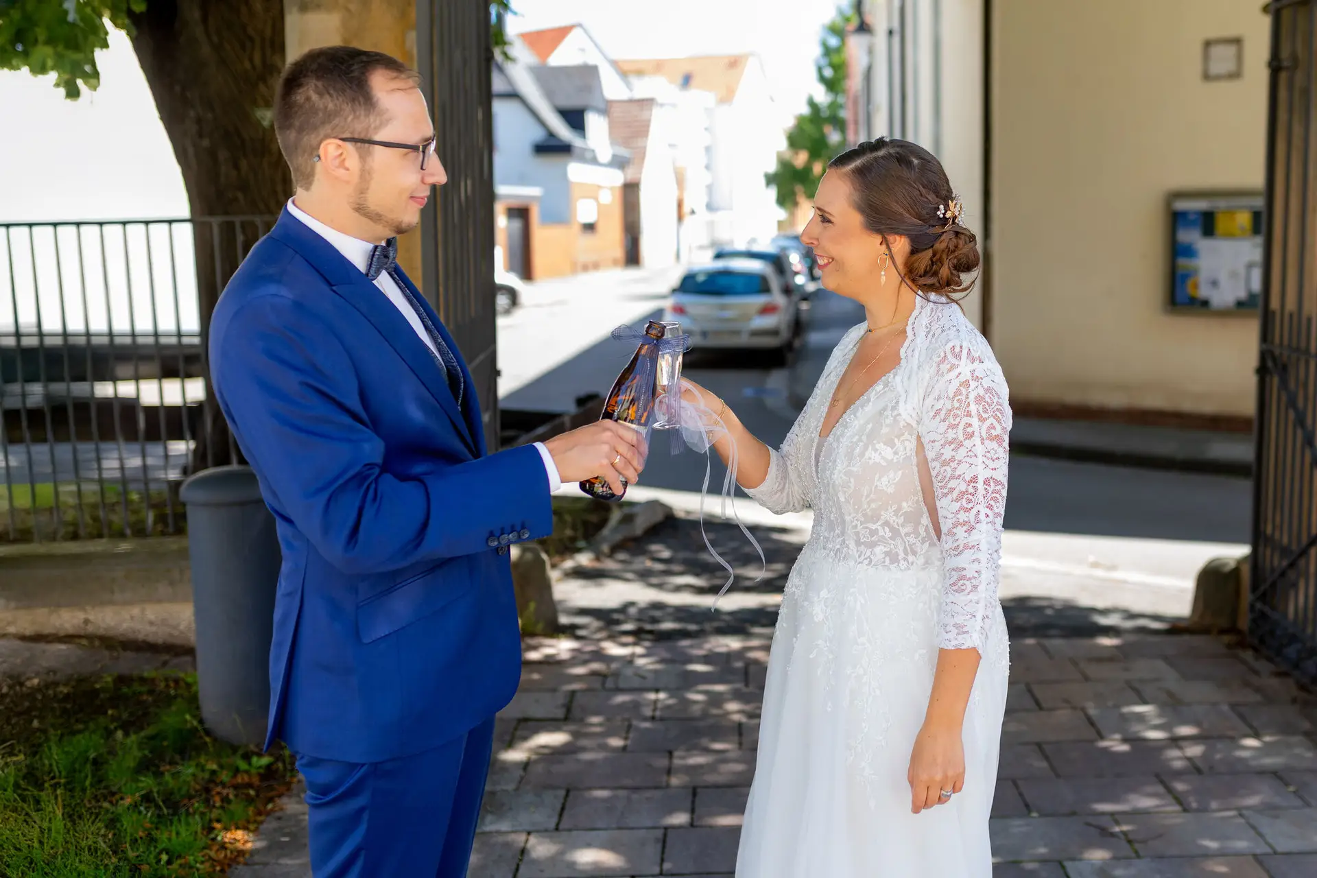 Braut und Bräutigam stoßen strahlend mit Champagner unter einem Baum auf der Straße nach der Trauung an