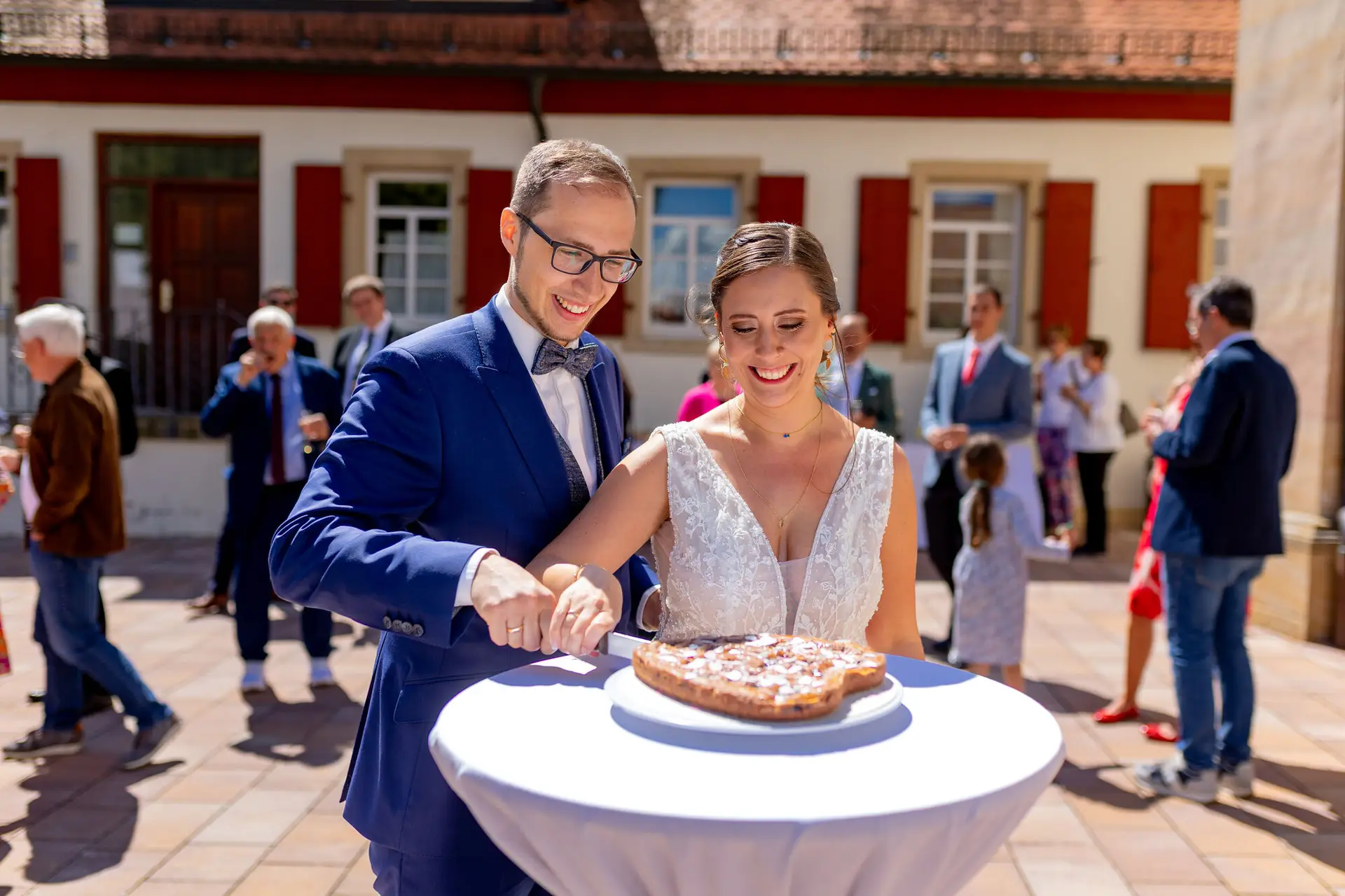 Brautpaar schneidet lachend die Hochzeitstorte vor der Kirche in Mutterstadt