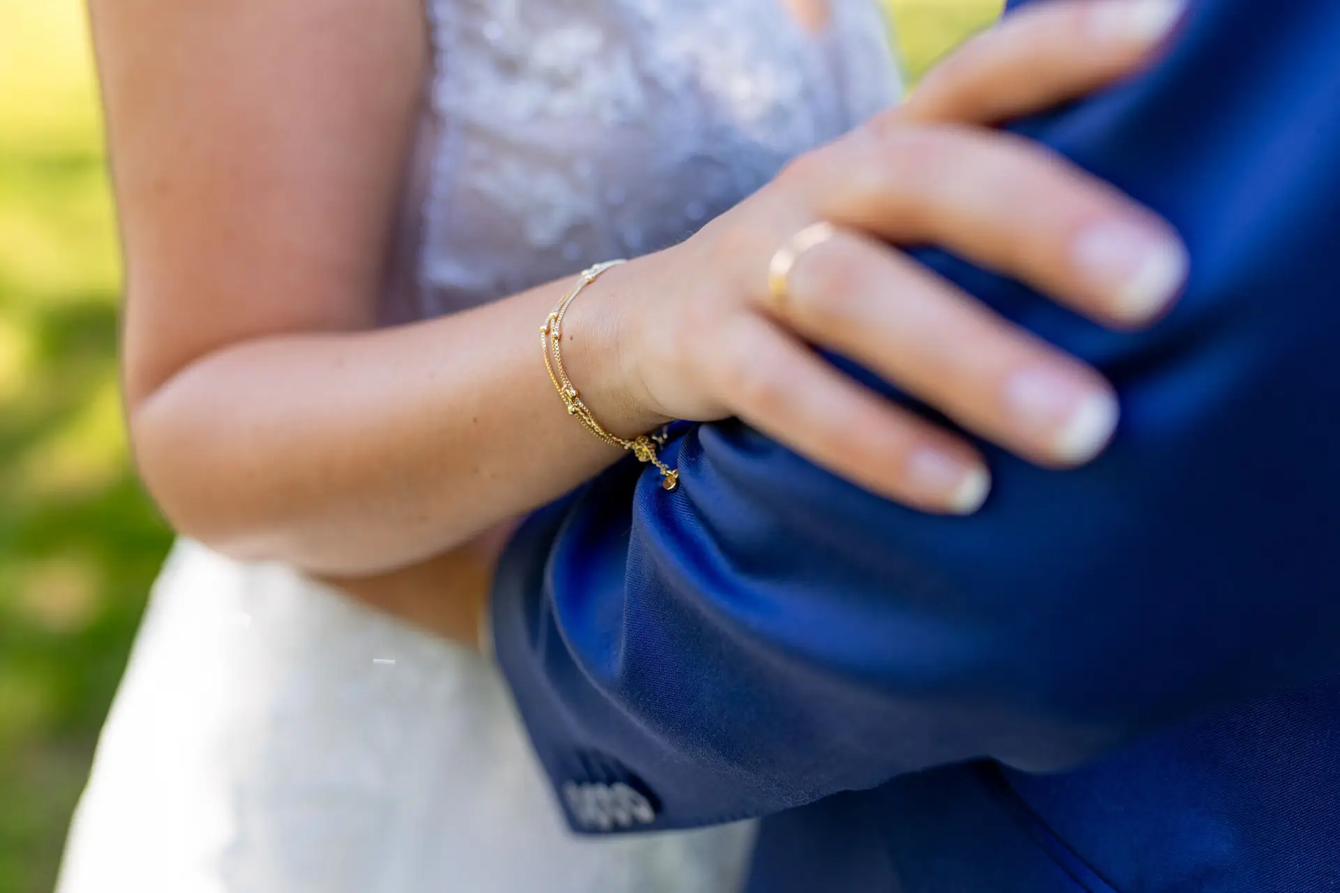 Nahaufnahme der Hand der Braut mit goldenem Armband auf dem Arm des Bräutigams im blauen Anzug