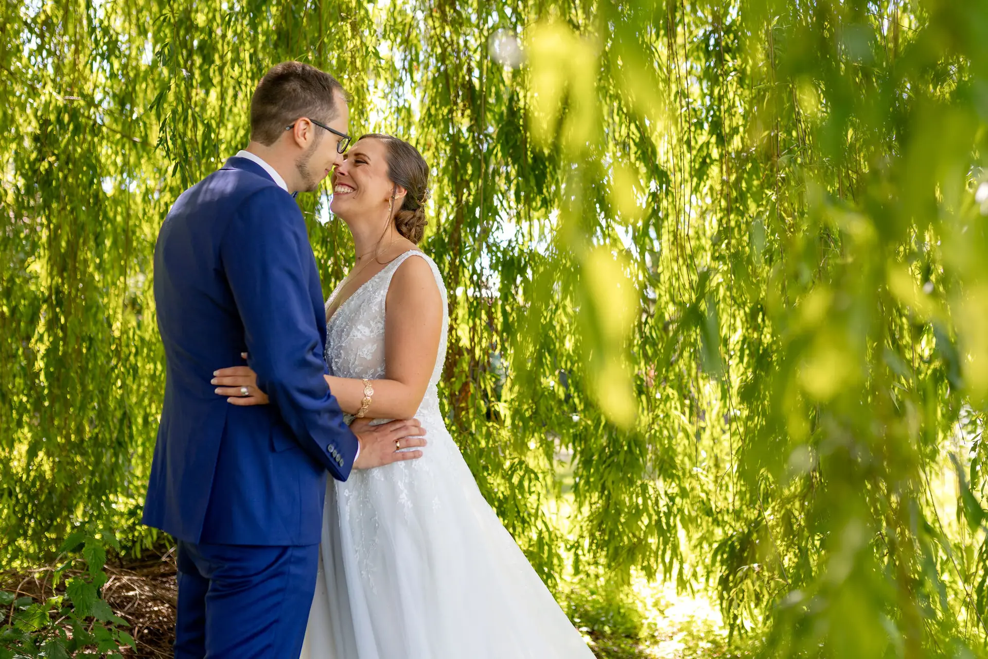 Brautpaar umarmt sich zärtlich unter einem Weidenbaum beim Brautpaarshooting