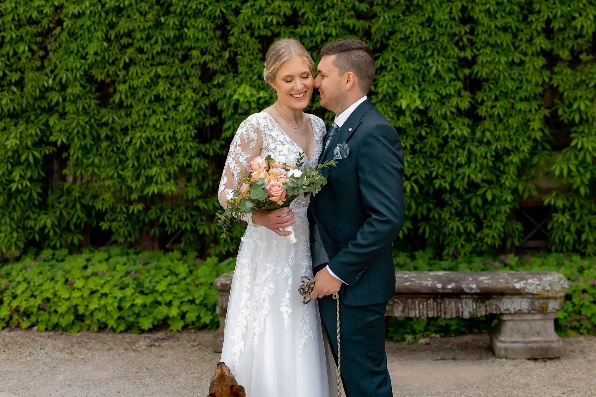 Brautpaar vor efeubedeckter Steinmauer im Schlossgarten Herrnsheim, Bräutigam küsst Braut auf die Wange