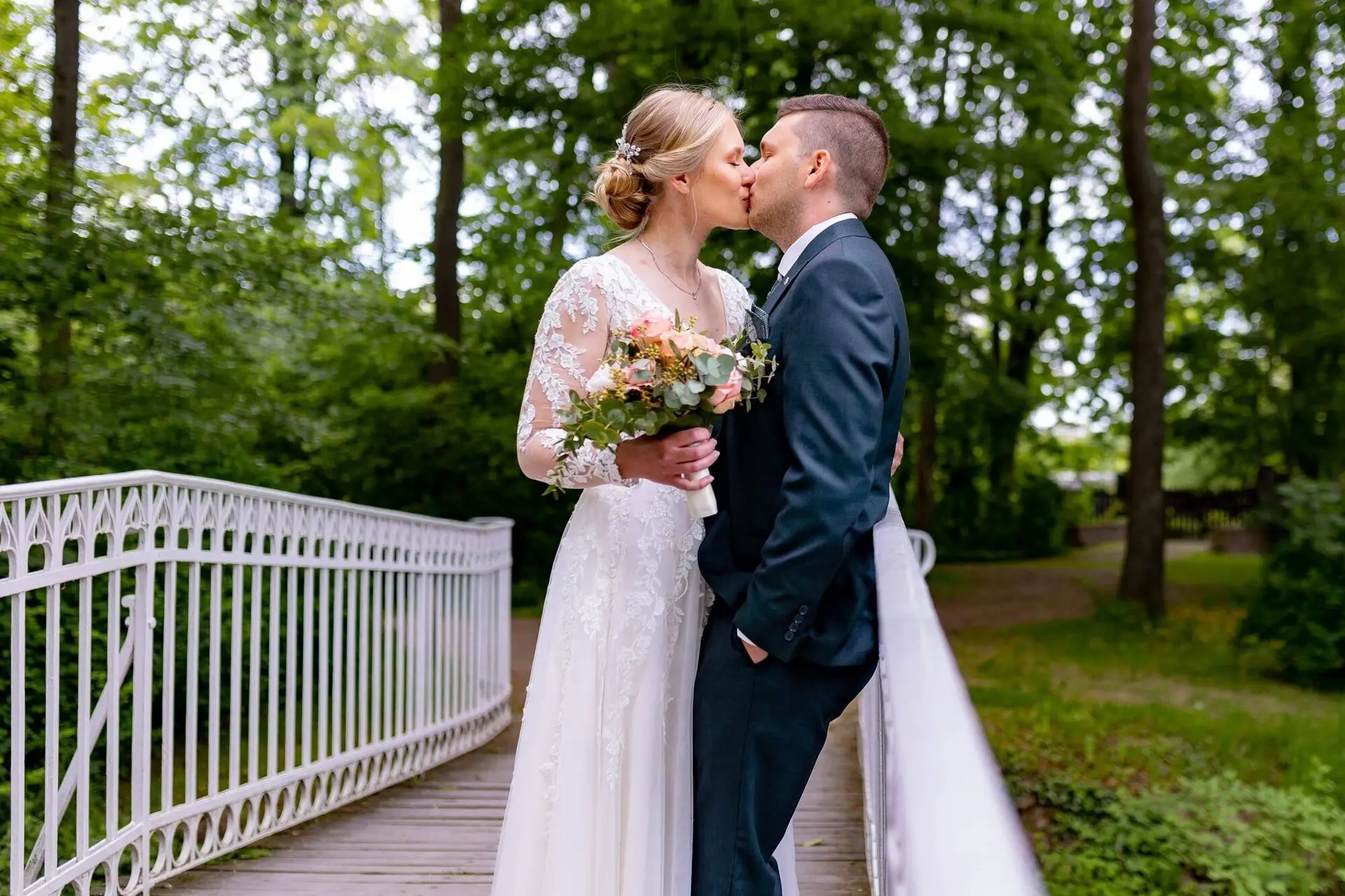 Brautpaar küsst sich auf der weißen Brücke im Schlossgarten Herrnsheim, umgeben von dichtem Grün