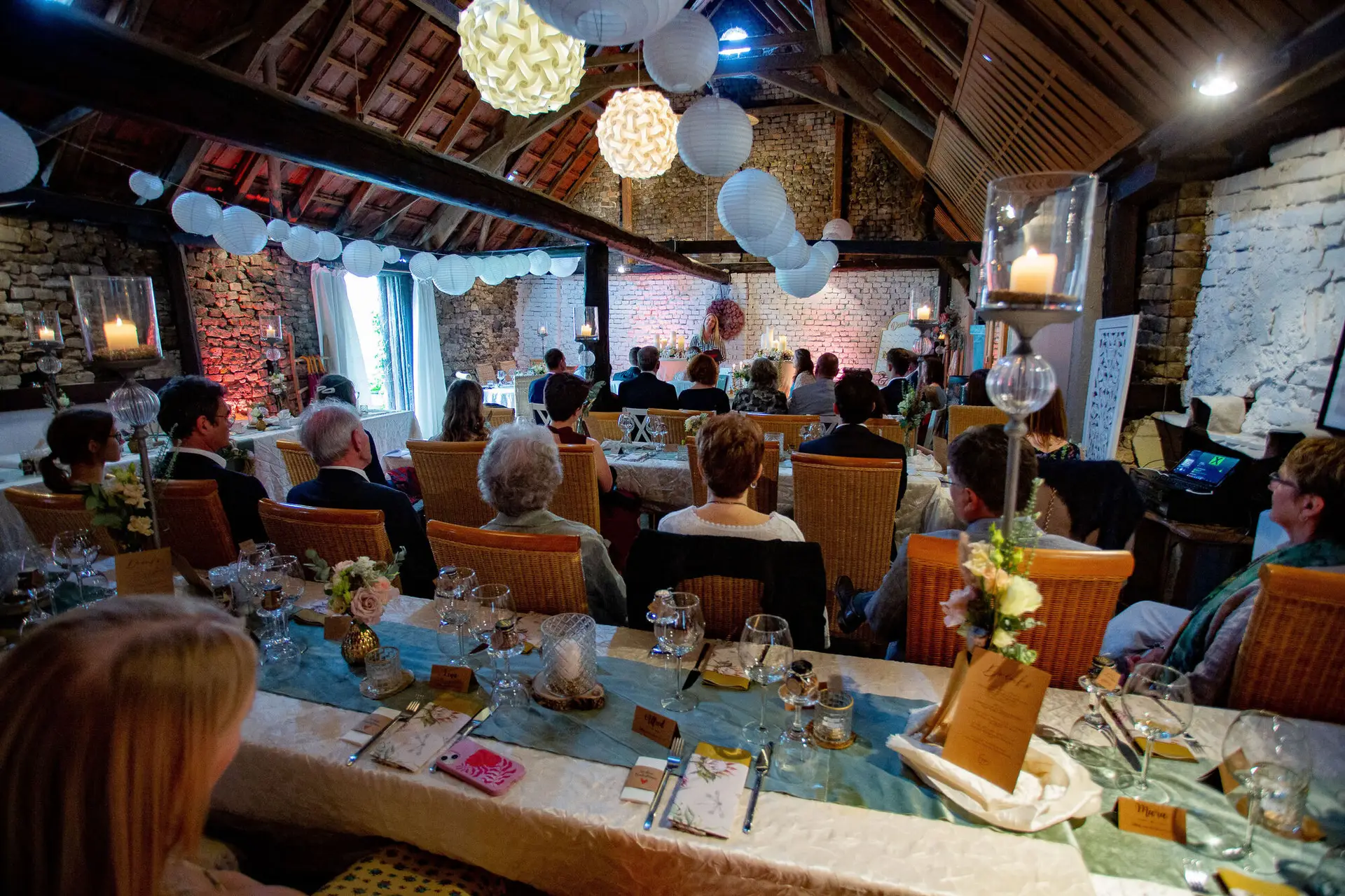Stimmungsvolles Hochzeitsdinner im strohgedeckten Festsaal mit Papierlaternen und Kerzenlicht, viele Gäste am langen Tisch