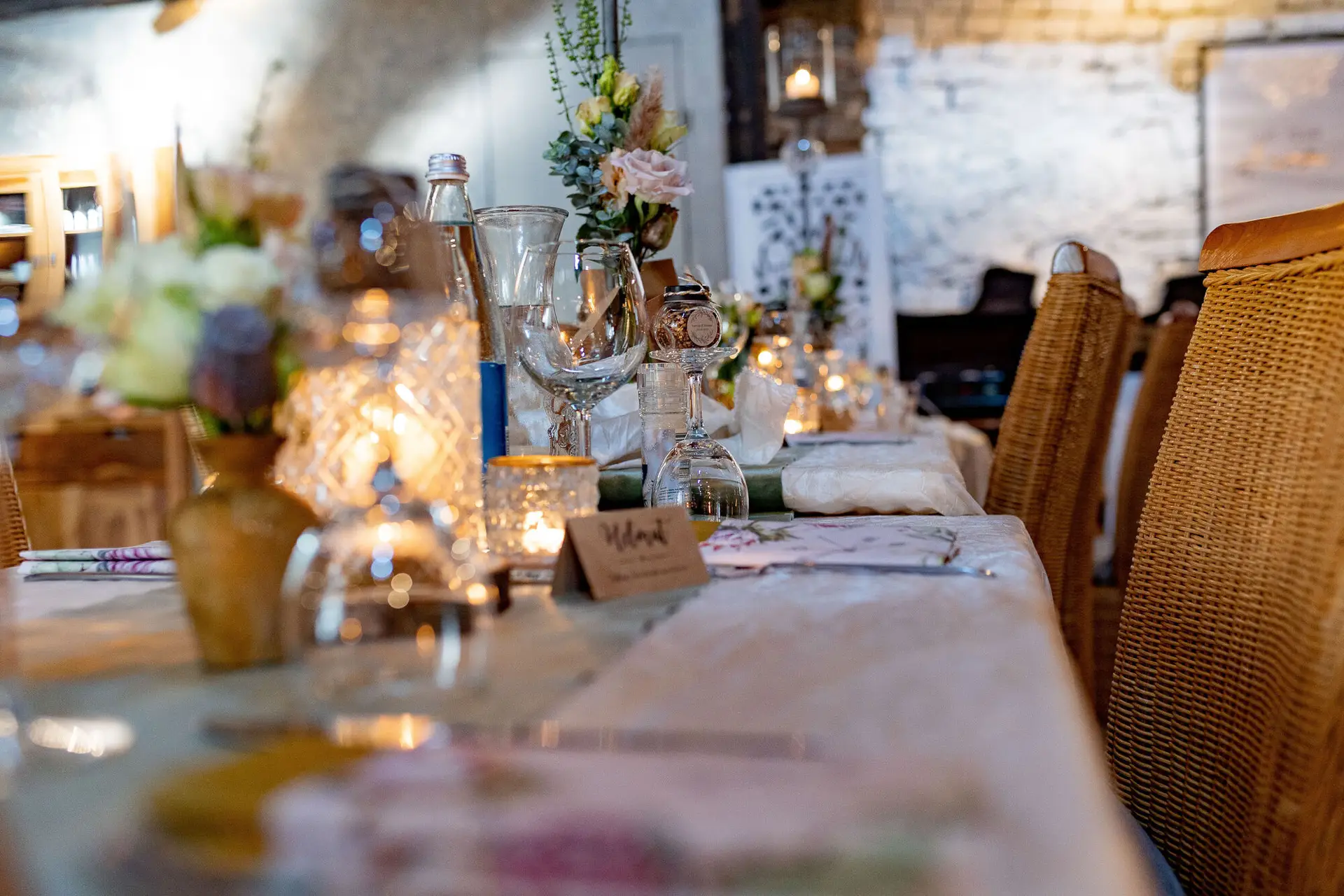 Langer Festtisch mit Blumenarrangements, Champagnergläsern und Kerzenlicht vor der rustikalen Ziegelwand