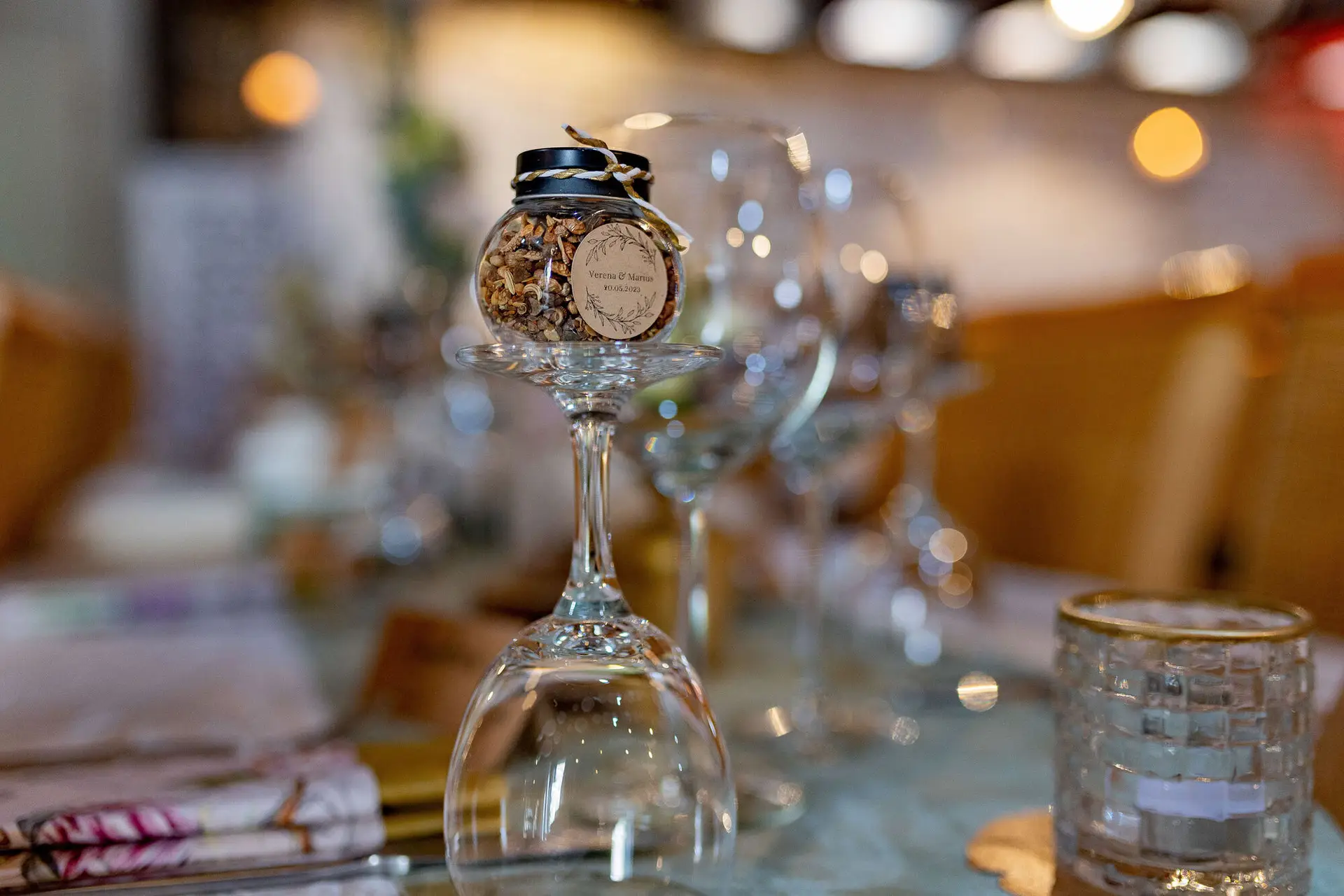 Gastgeschenk im kleinen Glas auf einem umgedrehten Weinglas – personalisierte Hochzeitsdekoration im Dach der Welten