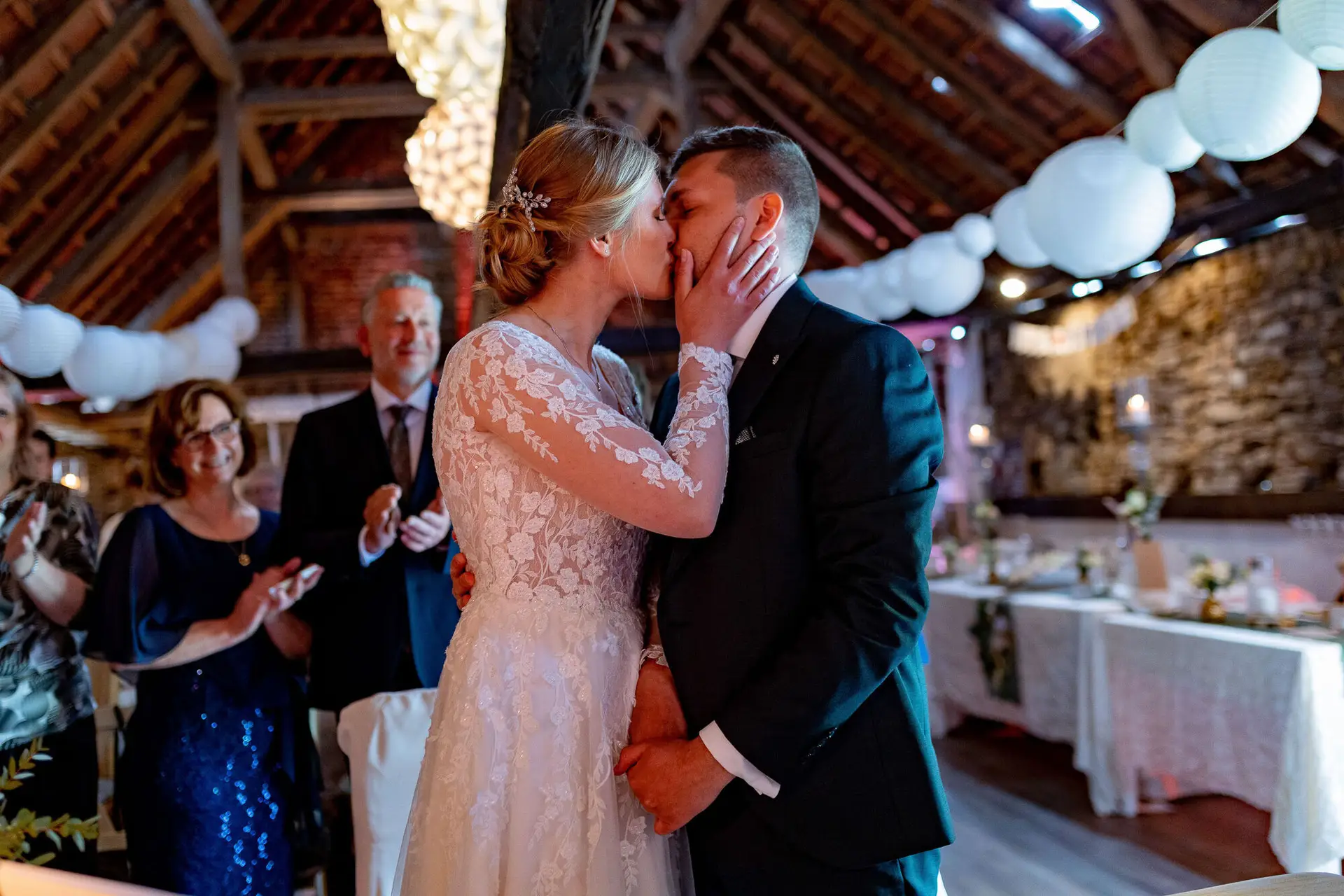 Brautpaar küsst sich vor den jubelnden und klatschenden Gästen im rustikalen Festsaal des Dach der Welten