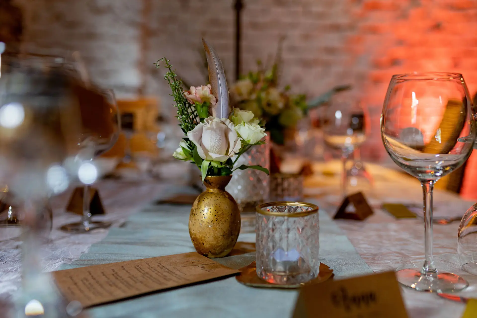 Tischdetail mit Menükarte, Blumenvase, Kerze und Weinglas vor der charakteristischen Backsteinwand