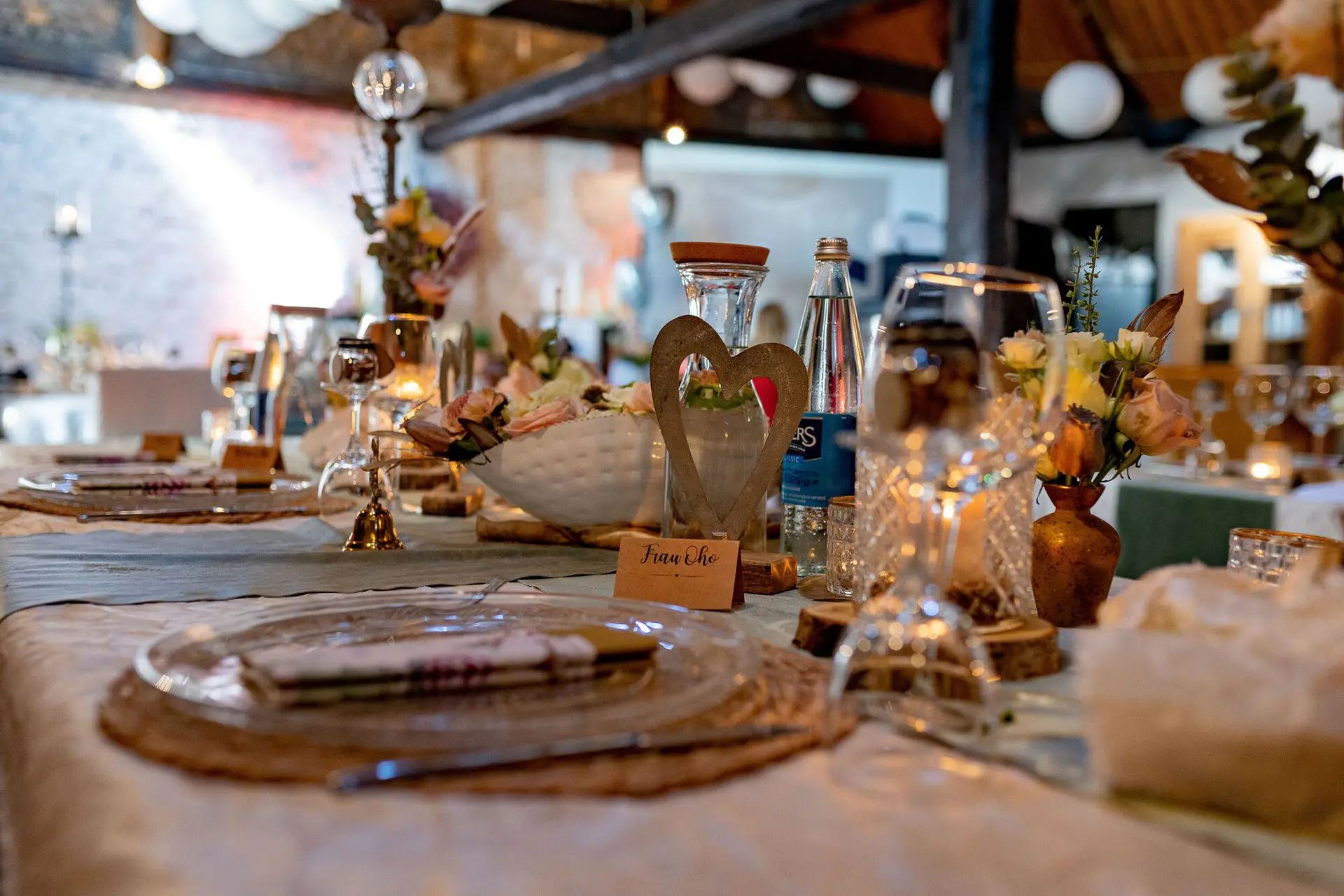 Gedeckter Tisch mit Blumendekoration in rustikal-charmantem Saal mit Ziegelwänden und Holzbalkendecke
